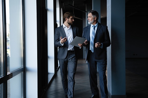 Two colleagues communicating in corridor, partners walking in the modern office.