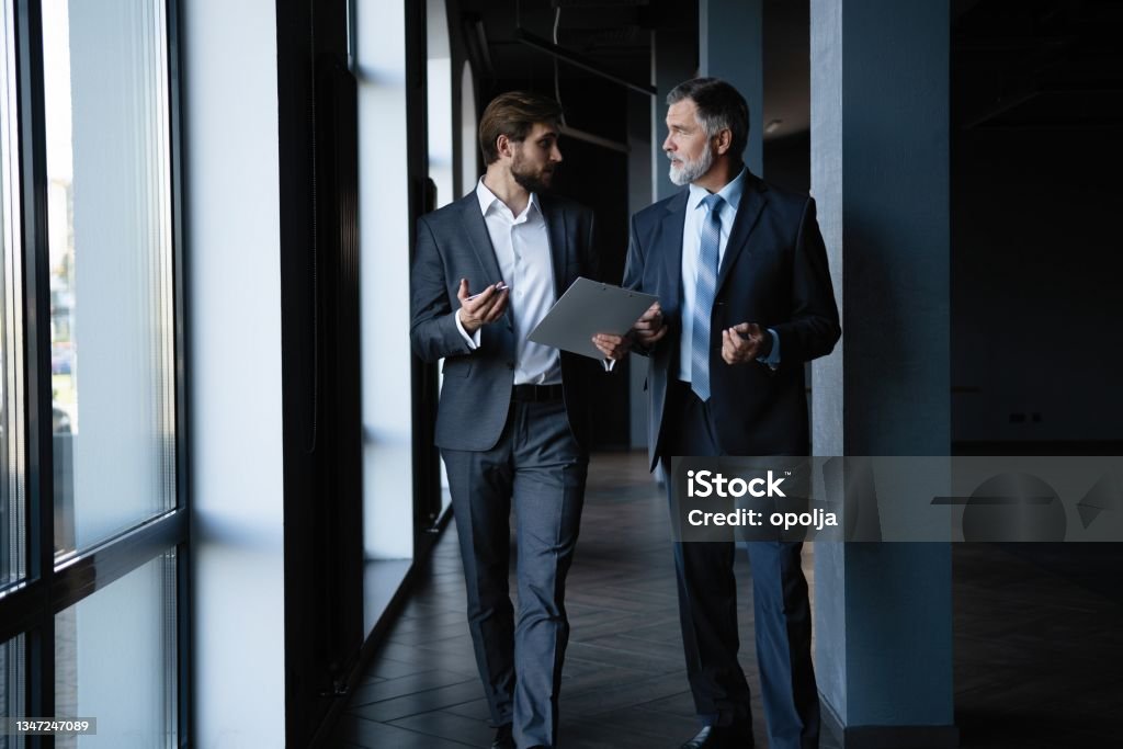 Two colleagues communicating in corridor, partners walking in the modern office Two colleagues communicating in corridor, partners walking in the modern office. Businessman Stock Photo