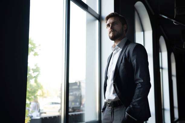 istock Confident young businessman looking at camera while standing near the window an office building. 1347249173