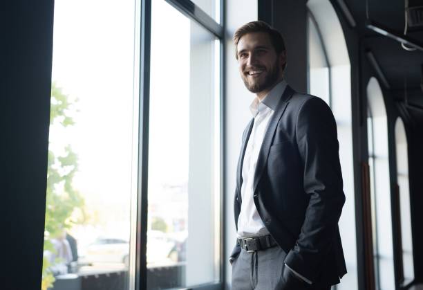 istock Confident young businessman looking at camera while standing near the window an office building. 1347249174