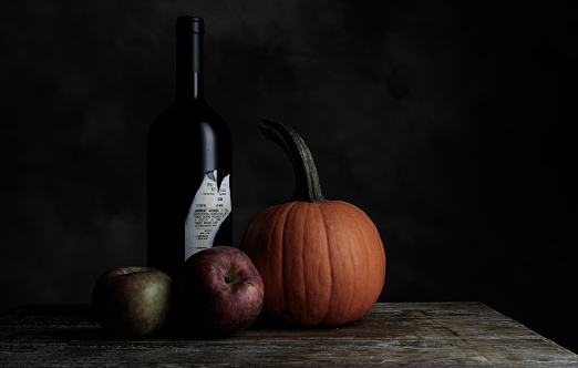 Apples, a pumpkin, a bottle of wine in low light