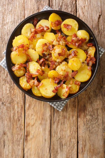 German fried potatoes with bacon and onions close-up in a plate on the table. vertical top view from above