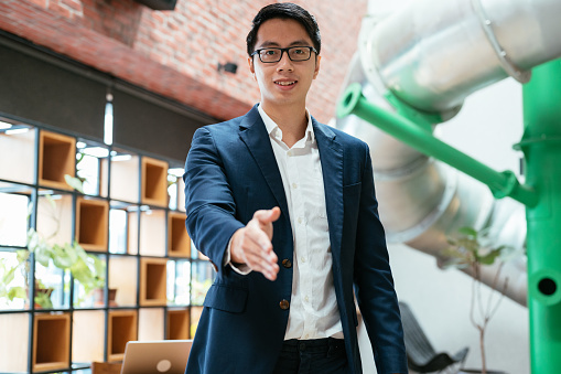 Young Asian businessman reaching out his hand for a handshake in a co-working space.  Return to work concept.