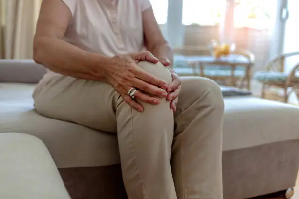 Old senior adult woman female hands touching knee sitting alone. Retired elderly grandma feeling hurt joint pain in leg suffering from osteoarthritis bones disease or injury concept, close up.