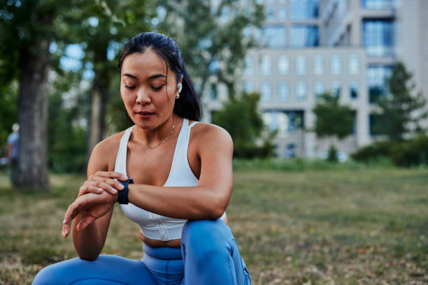 Beautiful sportswoman setting up smart watch during workout in park Female athlete setting up smart watch before workout in a forest. Beautiful asian sportswoman checking data on her gadget outdoor. active lifestyle stock pictures, royalty-free photos & images