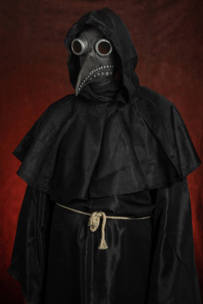 Dark black figure of a man in a mask of plague doctor stands on red background Dark black figure of a man in a mask of plague doctor stands on red background black plague doctor stock pictures, royalty-free photos & images