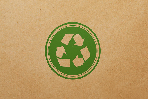 Green recycling stamp sitting over brown paper background. Horizontal composition with copy space. Sustainability and renewable energy concept.
