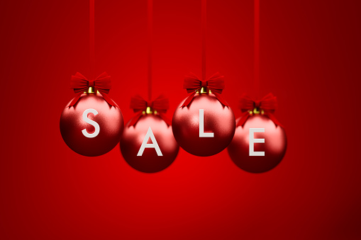 Sale written over red Christmas baubles hanging over red background. Christmas and festivity concept. Horizontal composition with selective focus and copy space.