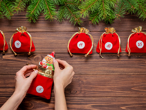 Advent calendar. Red bags with gifts on a wooden background. Hands are holding a gift.