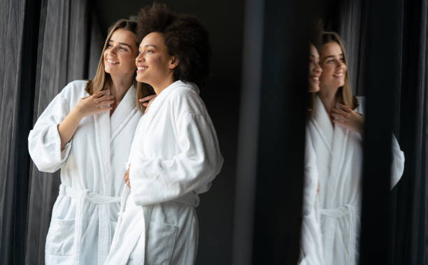 pareja de lesbianas relajándose y bebiendo té en batas durante el fin de semana de bienestar - bathrobe women cup towel fotografías e imágenes de stock