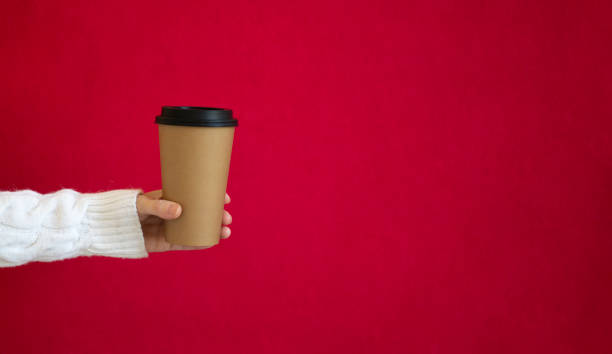 istock A woman in a white sweater holds a paper cup for coffee, on a red background 1347292921