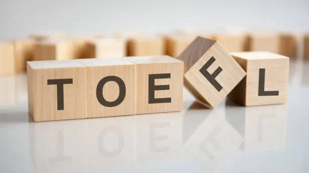 word TOEFL on wooden cubes, gray background. Reflection on the mirrored surface of the table. Test of English as a Foreign Language