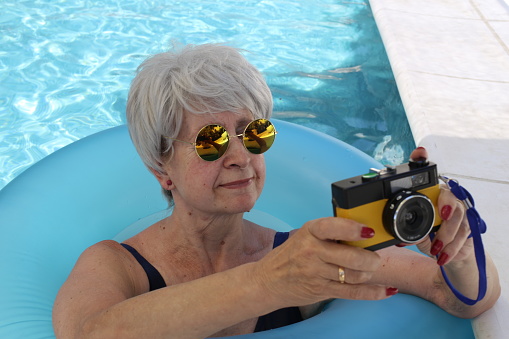Senior lady using vintage camera in resort pool.