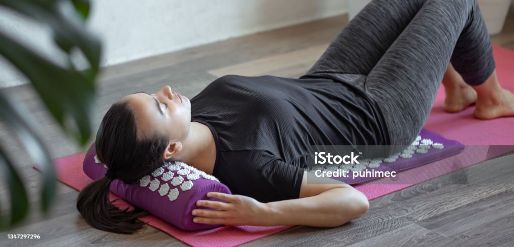 Young woman on acupressure mat in home acupuncture massage. A woman lies on a purple acupuncture massage pillow and a mat with white massage tips. Shiatsu Stock Photo