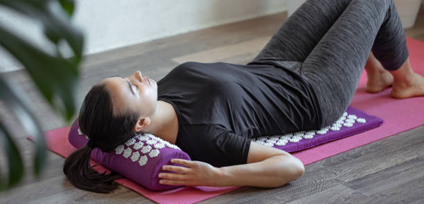 Young woman on acupressure mat in home acupuncture massage. A woman lies on a purple acupuncture massage pillow and a mat with white massage tips. acupuncture mat stock pictures, royalty-free photos & images