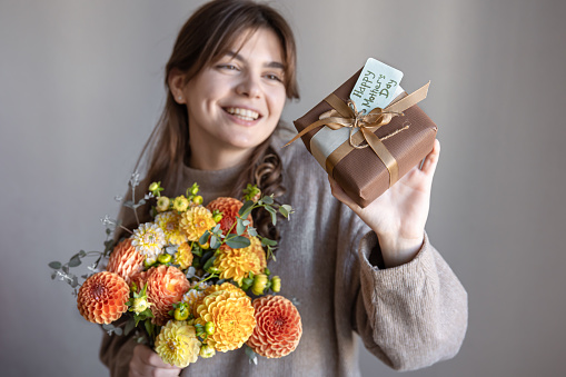 Attractive young woman with a mother's day gift and a bouquet of chrysanthemum flowers in her hands.