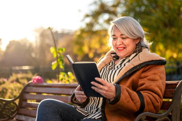 istock Mature woman reading a book at a park 1347298615