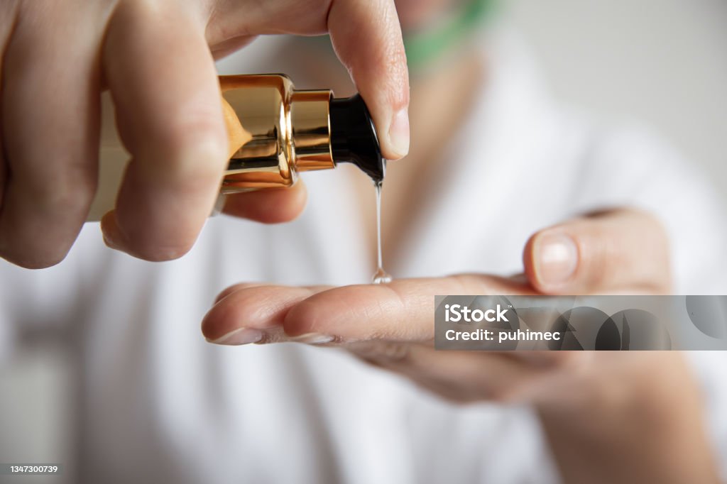 A woman presses on the dispenser of beauty care products, blurred background. Close-up, a woman in a white robe presses on the dispenser of beauty care products, blurred background. Moisturizer Stock Photo
