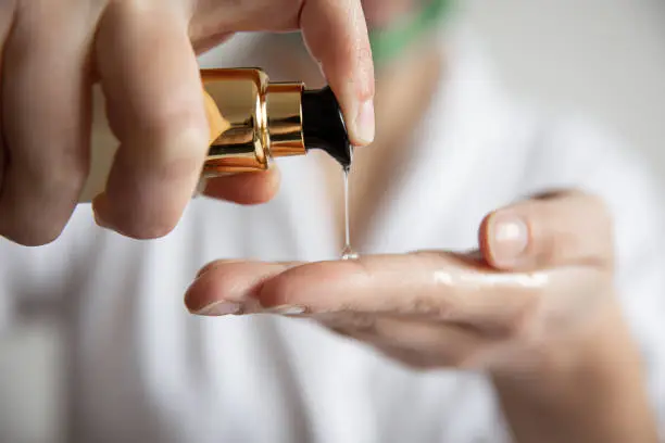 Photo of A woman presses on the dispenser of beauty care products, blurred background.