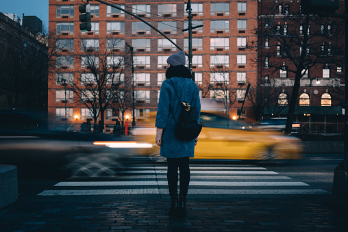 Back view of a young woman with backpack waiting for green traffic light while standing at the Chelsea district, New York City , USA