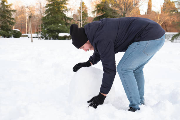 istock Young caucasian man rolling a big snowball to make snowman 1347303476