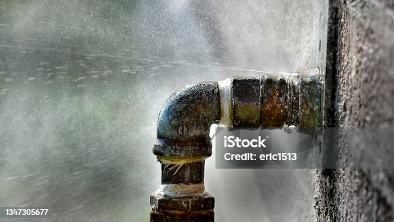 istock Old rusty pipe with leak and water spraying out under pressure leaky leaking 1347305677