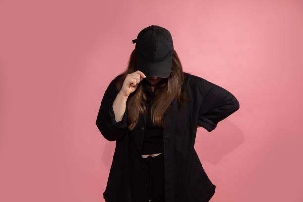 istock Young unrecognizable woman in black baseball cap lowered head down. Mock-up, copy space. Sportswear, pink background, studio shot. 1347305909
