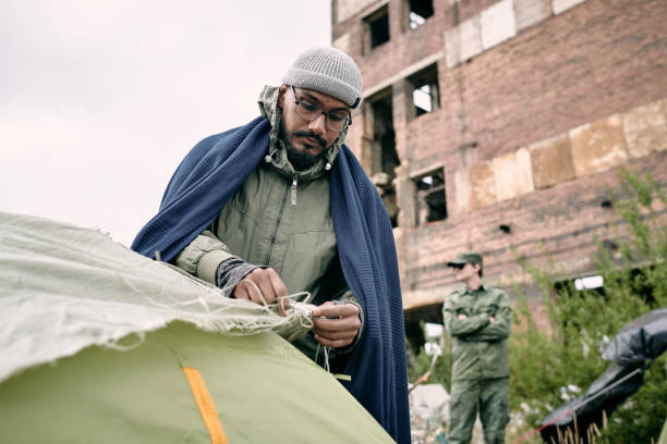istock Male refugee pitching tent against half ruined building 1347306059