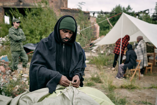 istock Young male migrant pitching tent in refugee camping 1347306078