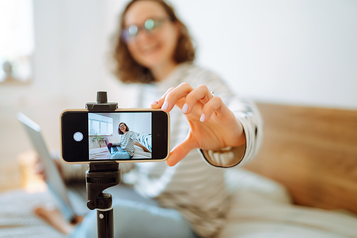 Video blog. Young woman looking into the camera and telling her story while leading a video blog. Vlogger makes online streaming using phone. Social media, instagram, stay home and quarantine.