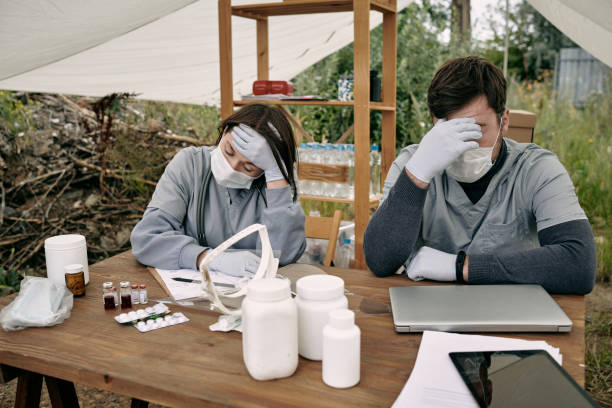 istock Two young exhausted clinicians in protective workwear sitting by table 1347306326