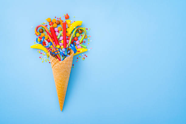Overhead view of a waffle ice cream cone filled with multicolored candies shot on blue background. The composition is at the left of an horizontal frame leaving useful copy space for text and/or logo at the right.\n High resolution 42Mp studio digital capture taken with SONY A7rII and Zeiss Batis 40mm F2.0 CF lens