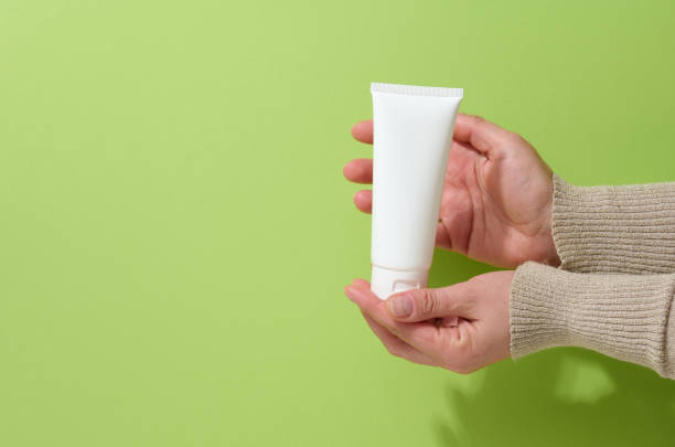 istock female hand holds empty white plastic tubes for cosmetics. Packaging for cream, gel, serum, advertising and product promotion 1347314102