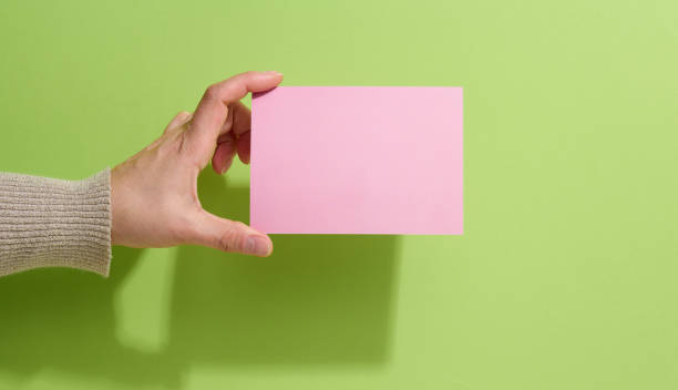 istock Female hand holding empty pink paper on a green background. Copy paste image or text, close up 1347314692