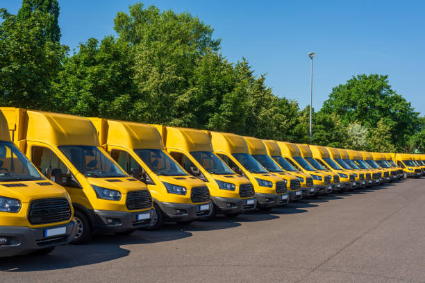 A fleet of electric yellow delivery vans are parking in front of green trees. stock photo