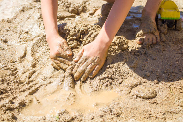 barfüßiger junge, der mit nassem sand spielt. kleiner junge knetet und modelliert schlamm an sommerlichen sonnigen tagen - lifestyles child beach digging stock-fotos und bilder