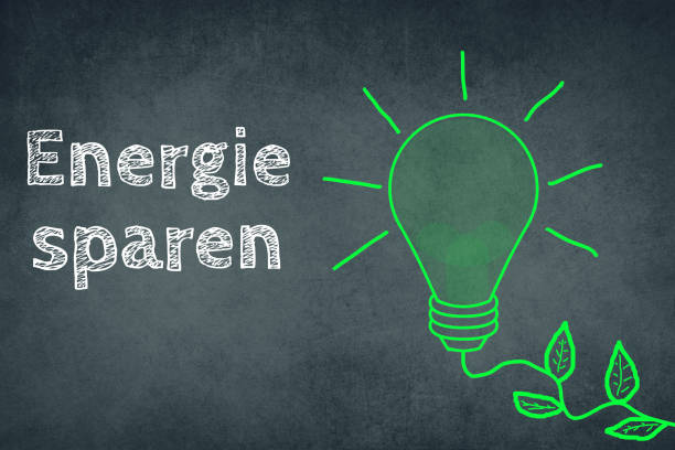 Saving energy is standing in german language on a chalkboard besides a green coloured light bulb, renewable technology stock photo