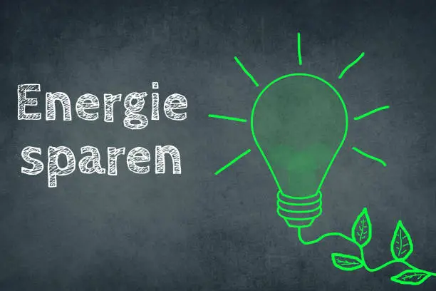 Saving energy is standing in german language on a chalkboard besides a green coloured light bulb, renewable technology, enviroment issues