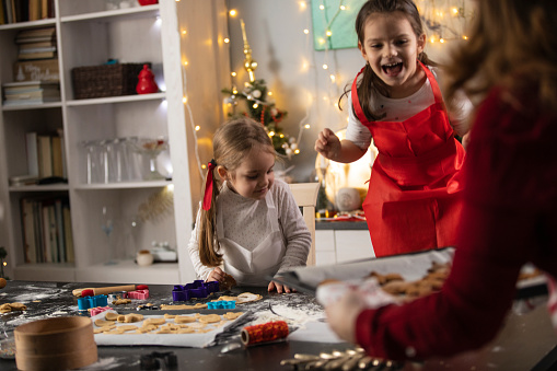 Candid shot of two little girls getting excited as their mother is bringing out a tray with a first batch of gingerbread cookies that finished baking.