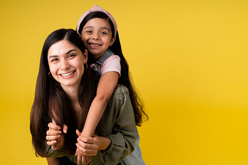 Portrait of an adorable little girl hugging her beautiful mother in front of a yellow background with copyspace