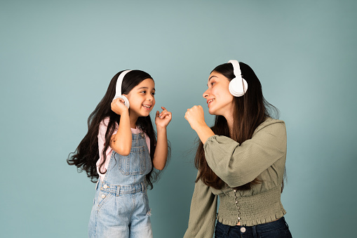 Sing with me. Hispanic young mom and little girl singing together while listening to music with headphones
