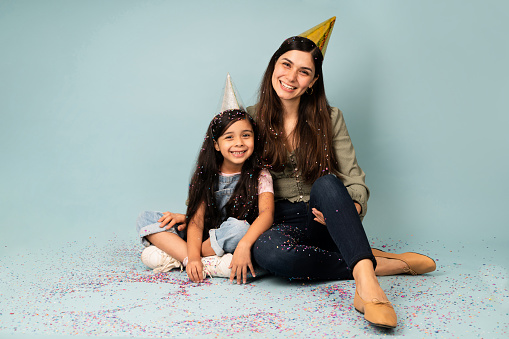 Beautiful young woman and little daughter celebrating a birthday party with confetti