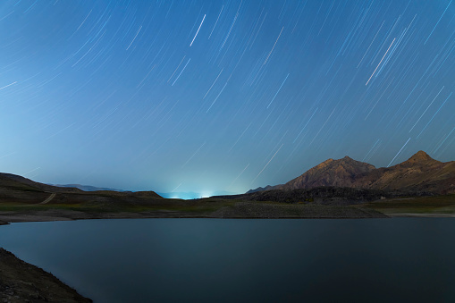 Beautiful long exposure night landscape. Small lake and mountains under star trails starry sky.