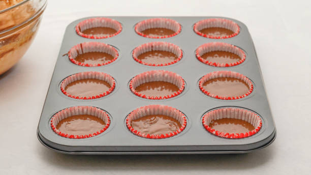 istock Chocolate muffins or chocolate cupcakes recipe. Lined cupcake pan with chocolate batter close up 1347336840