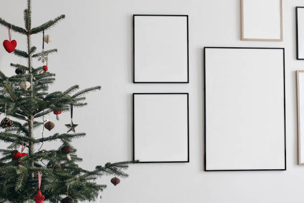 Christmas interior. Decorated fir tree with hanging traditional winter ornaments. Set of black and wooden portrait picture frame mockups. Wall art gallery. White wall background. Living rooom. stock photo
