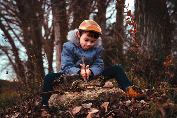 istock Boy in a blue coat is trying to light a fire in the field 1347347257