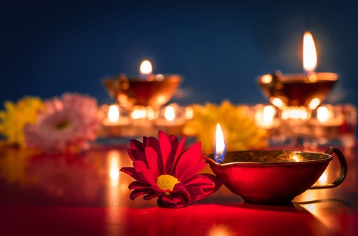 Happy Diwali. Burning diya oil lamps and flowers on blue background. Traditional Indian festival of light. Celebrating religious holiday.