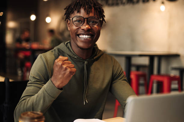 istock African man communicates on a laptop while sitting in the office, waving his hand gesture: success, victory 1347367709