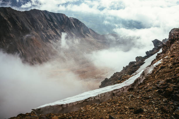 istock View from precipice edge with sharp rocks and snow cornice to mountain valley in low clouds. Wonderful mountain scenery with low clouds in highland valley. Scenic alpine landscape with rocky mountains 1347369267
