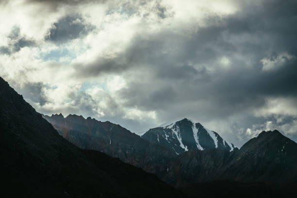 istock Atmospheric mountain landscape with silhouettes of rocks and snowbound sharp pinnacle under cloudy sky. Great rocks with snow. Beautiful mountain scenery with snow peaked top. Snow-capped pointy peak. 1347369276
